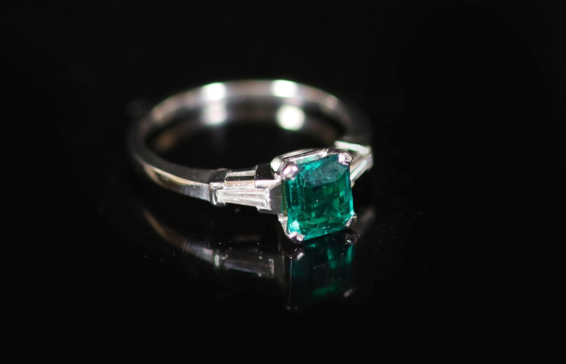 A platinum and single stone emerald ring with trapeze cut diamond set shoulders